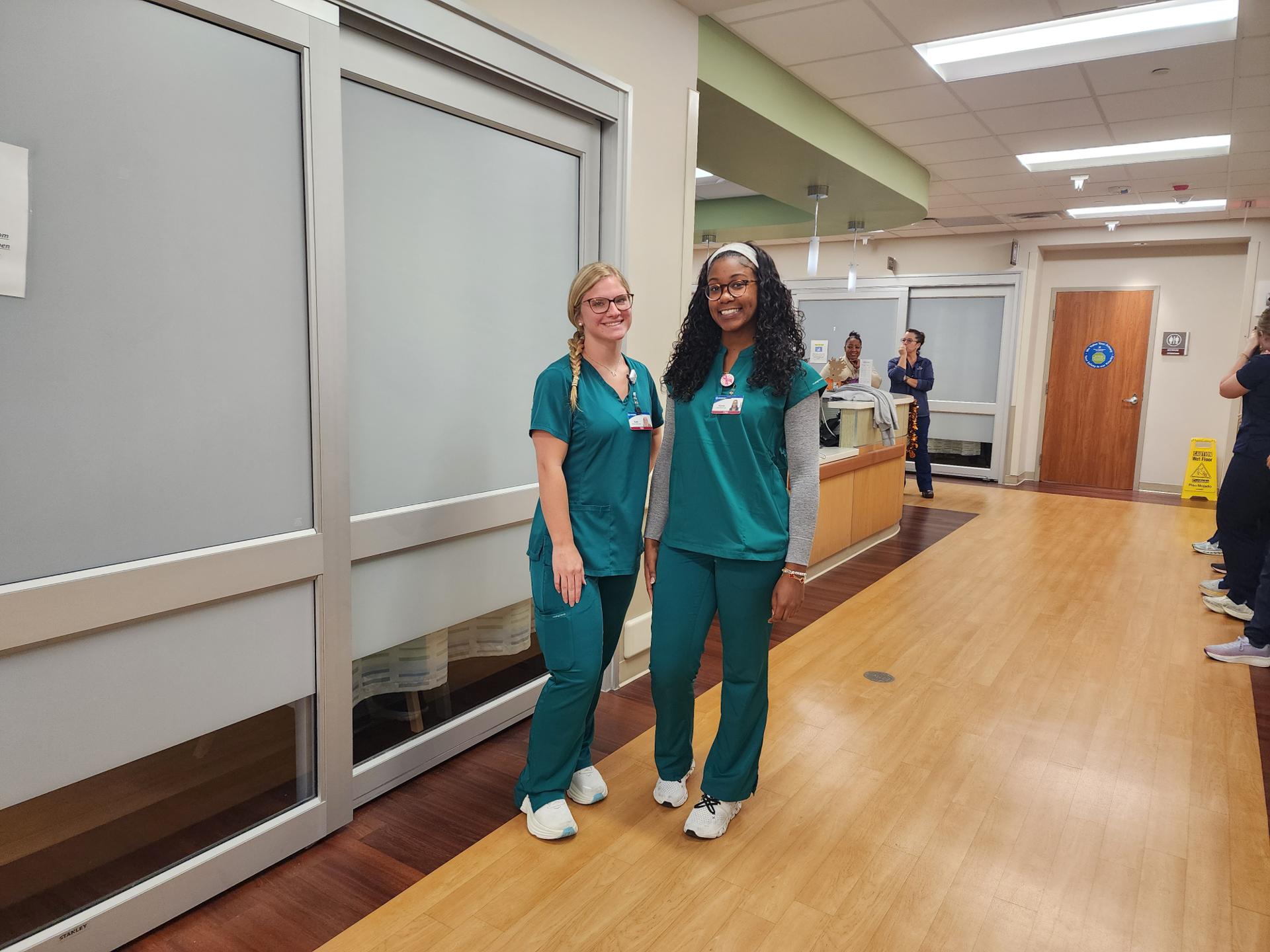 Two CRNA employees smiling for photo with others in the background.