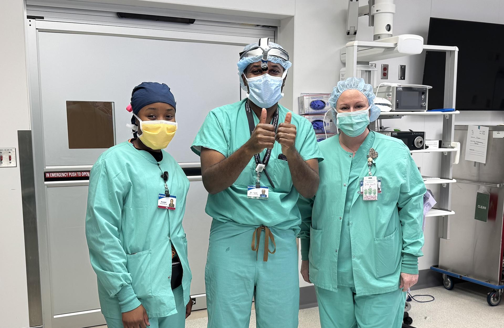 Three smiling surgery employees wearing masks with a doctor giving two thumbs up.