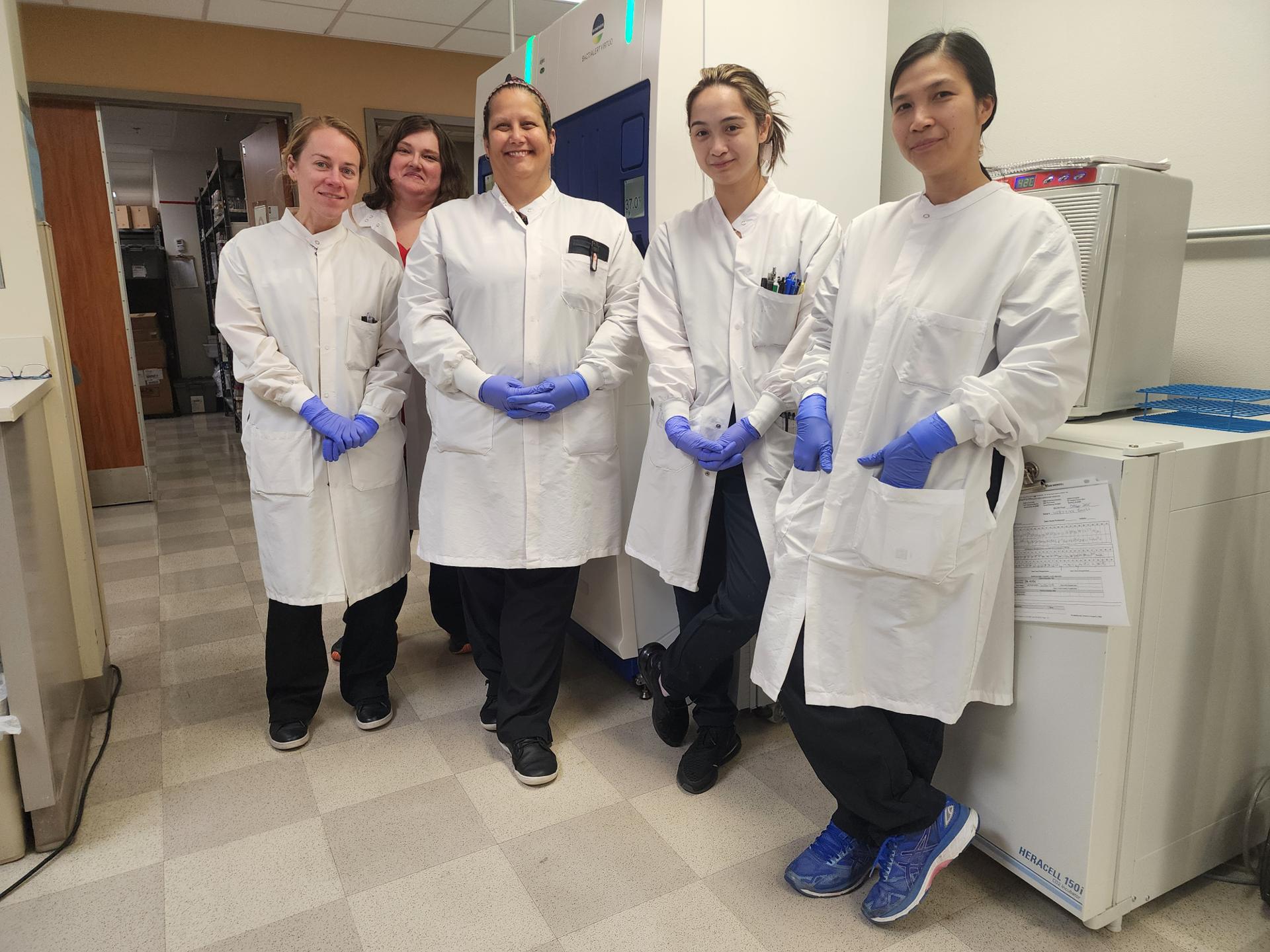 Five allied health employees wearing lab coats smiling.