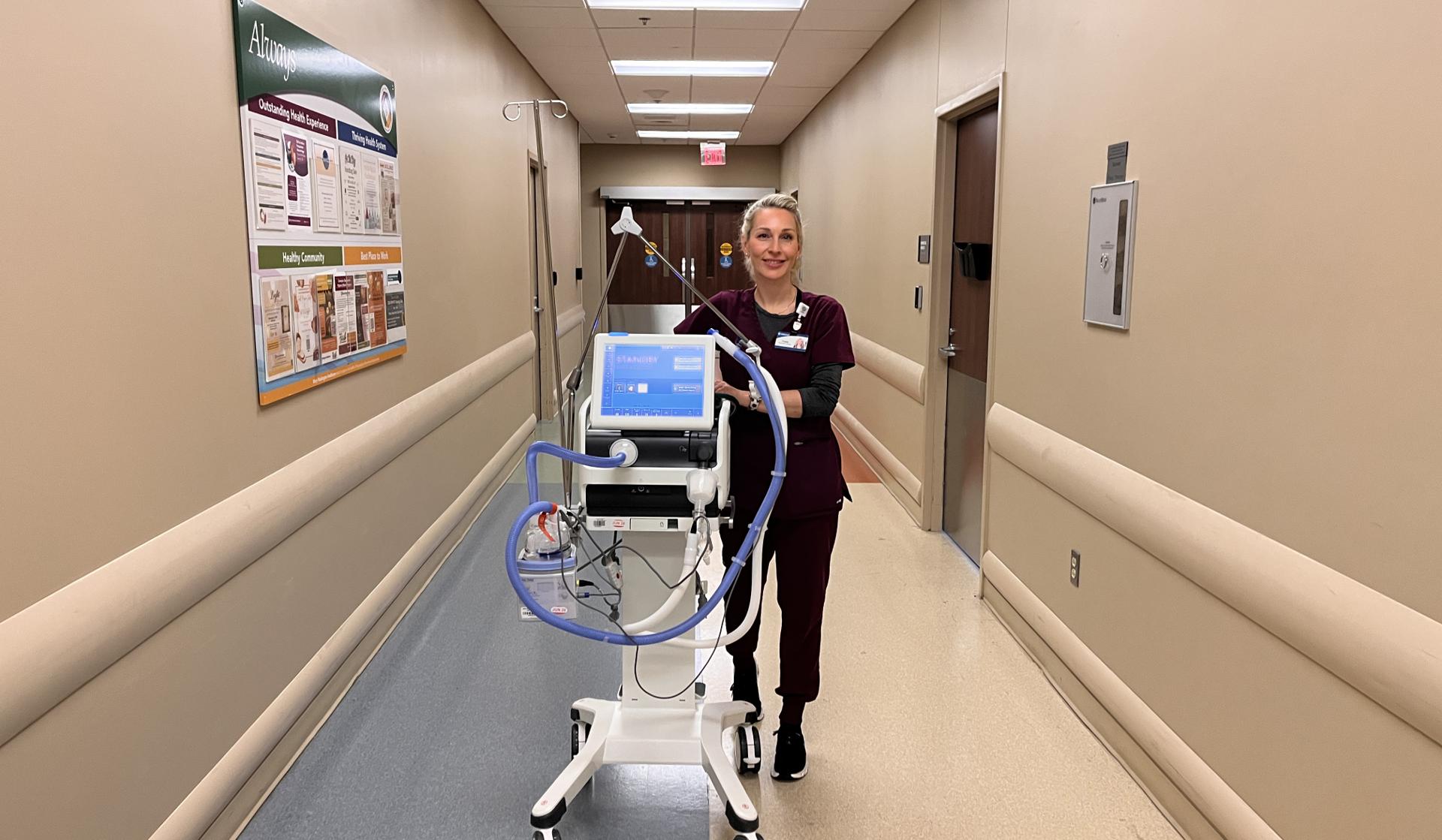 Employee transporting a mobile patient monitoring system through a hospital corridor.